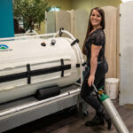 Emily Crockett standing in front of the hyperbaric oxygen therapy module at Nearing Total Health