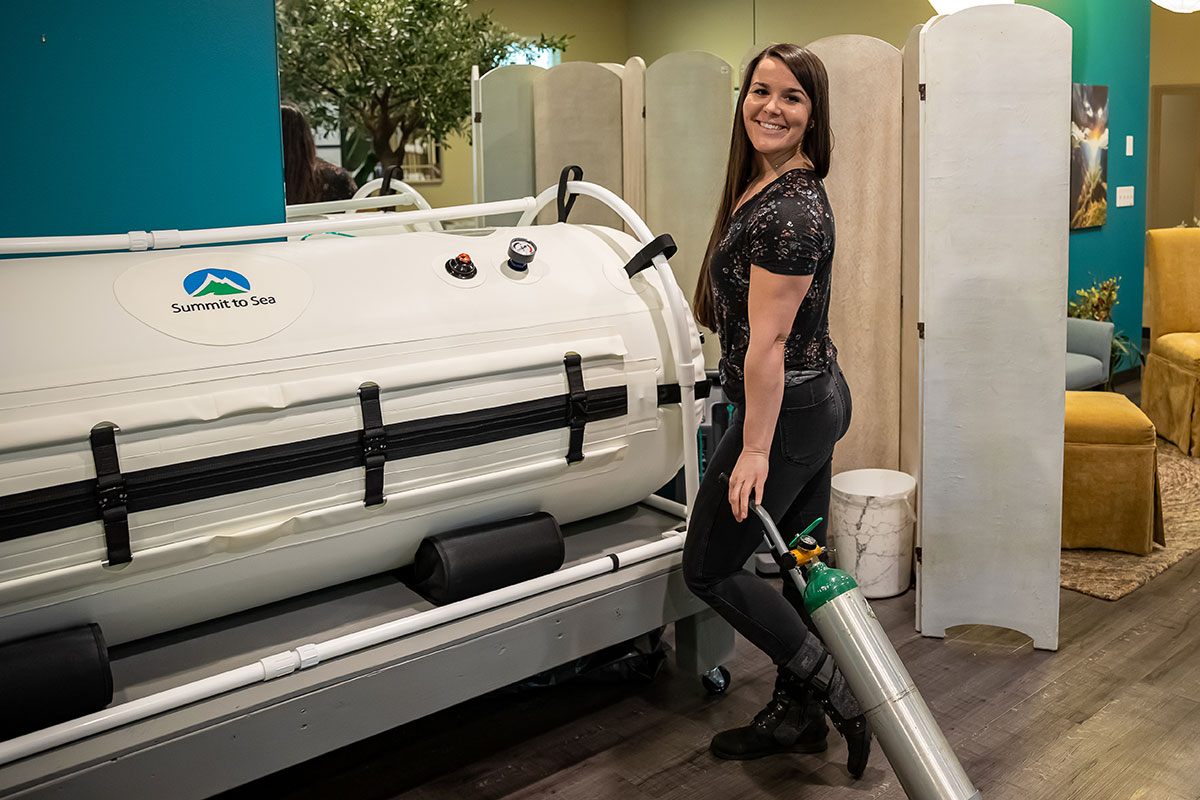 Emily Crockett standing in front of the hyperbaric oxygen therapy module at Nearing Total Health